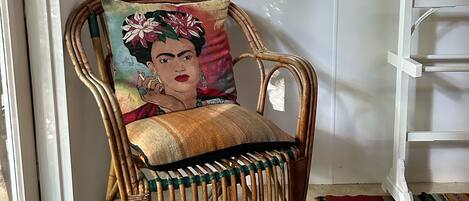Une chaise en osier avec un coussin, un tapis rouge et une carte encadrée accrochée au mur.