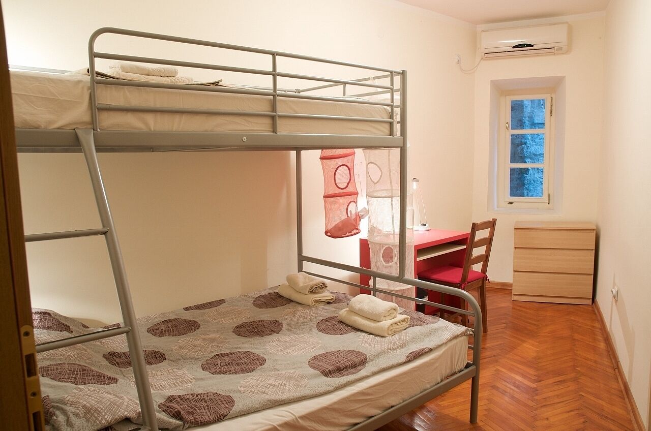 A bunk bed room with a desk and chair, a window, and a wardrobe.