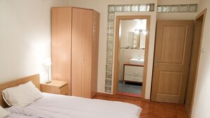 Une chambre à coucher comprenant un lit, une armoire, une table de chevet, un miroir et une salle de bain visible à travers une porte ouverte.