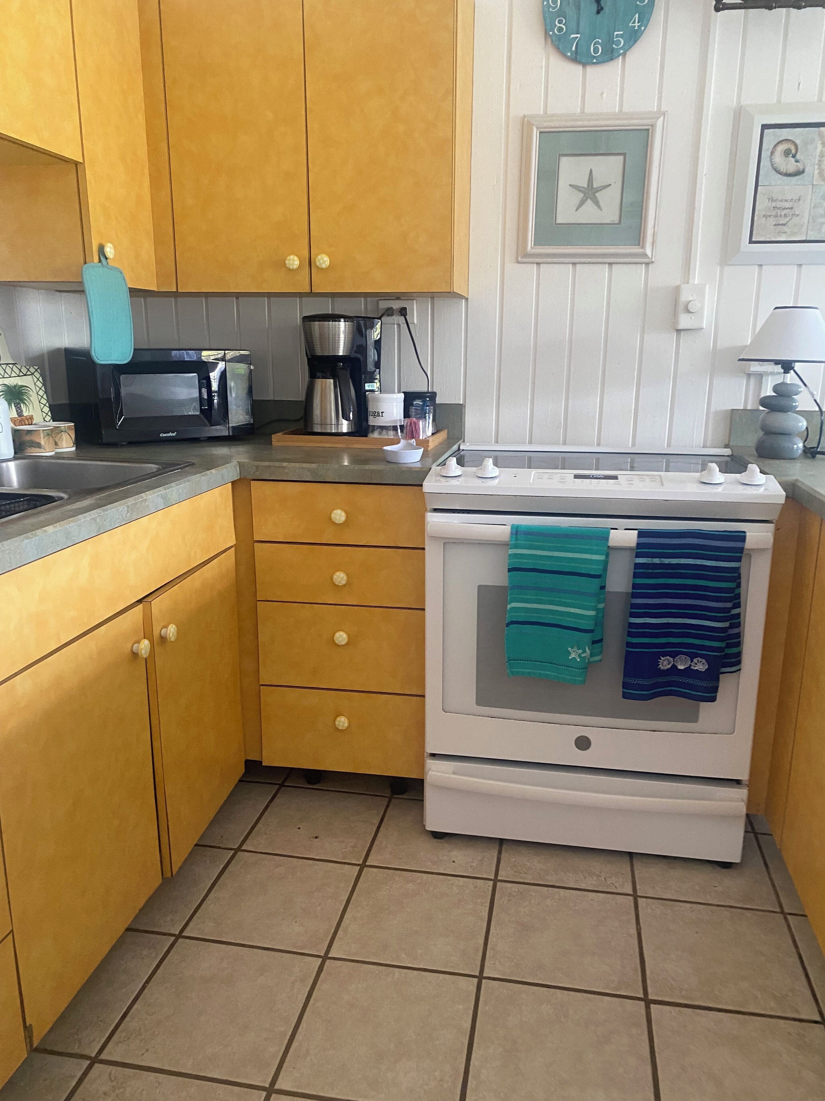 A compact kitchen with wooden cabinets, a microwave, a coffee maker, and a stove with towels hanging on the oven door.