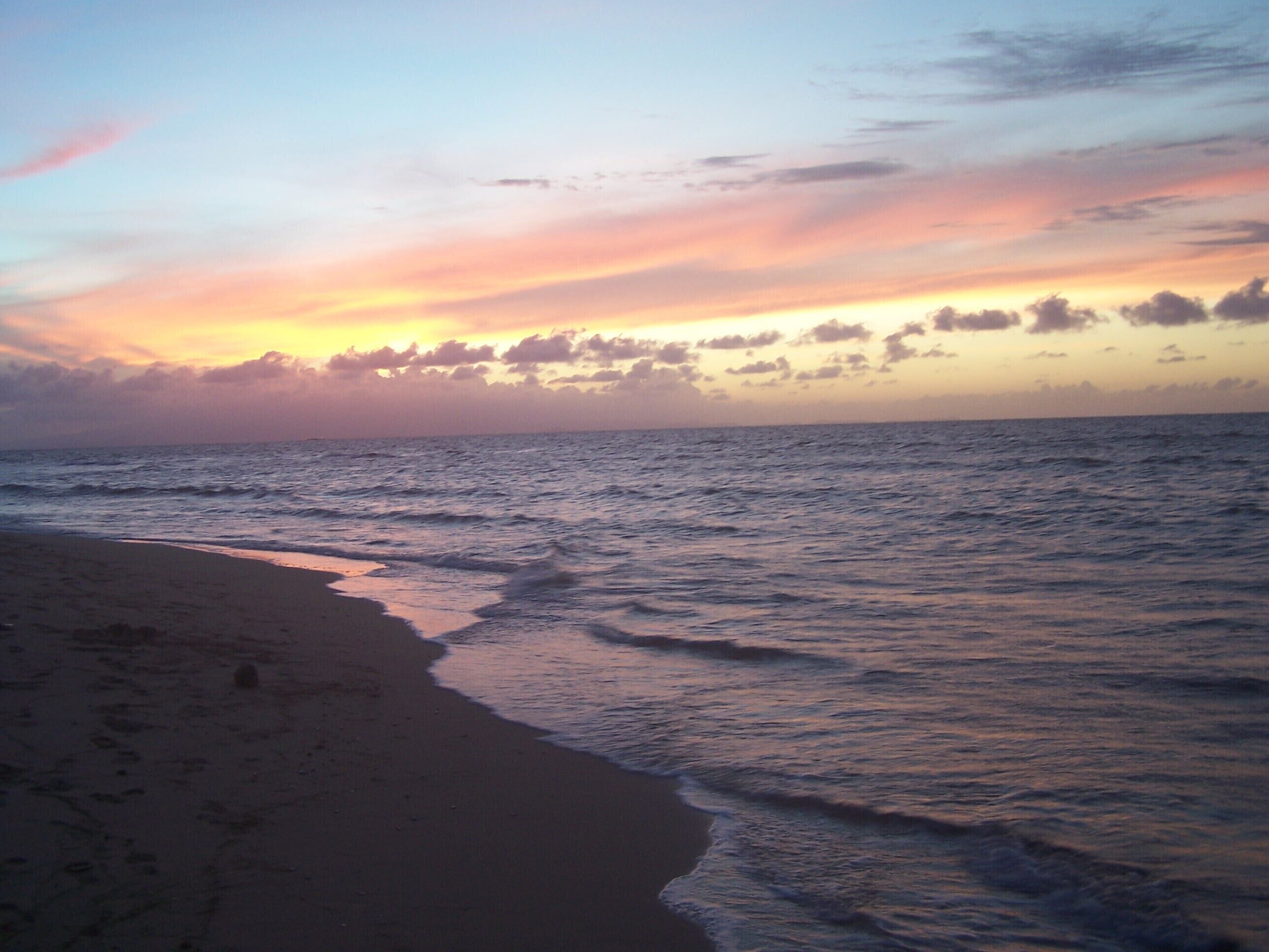 Ein Strand mit sanft anschwellenden Wellen unter einem Abendhimmel.