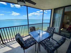 Ein Balkon mit einem Glastisch und vier gemusterten Stühlen, mit Blick auf ein klares blaues Meer und eine entfernte Küste.