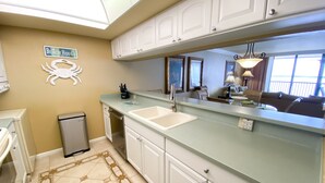 Una cucina con mobili bianchi, un lavello capiente e un piano di lavoro. Si nota una decorazione a granchio sulla parete e un cartello con scritto "Beach House".