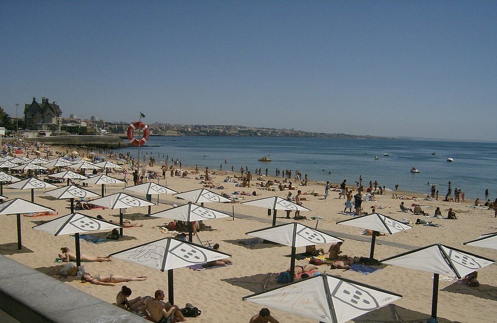 A beach with numerous umbrellas and people sunbathing.