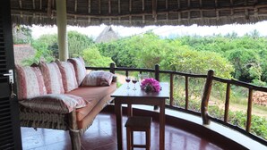 A thatched-roof veranda with a cushioned seating area and a table with a glass of red wine and flowers. - Luxurious villa w/pool,10min beach, 280m²,w/ personal & cook, Jacuzzi, A/C,wifi (Kenia)