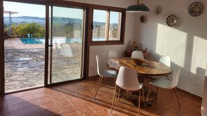 A dining area with a large table, chairs, and a view of a swimming pool and garden.