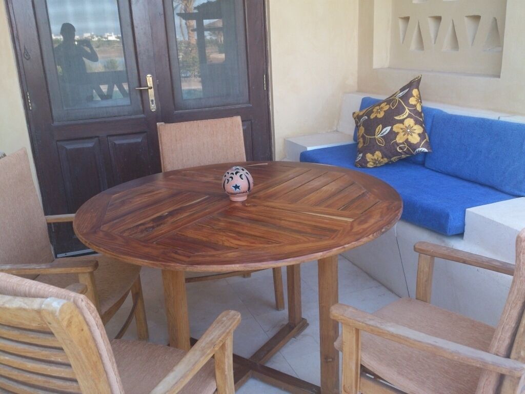 Ein runder Holztisch mit Stühlen, ein blaues Sofa mit blumigen Kissen und eine Tür mit satinierten Glasscheiben.