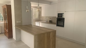 Une cuisine moderne avec un îlot central en bois, des armoires blanches, un four encastré et des luminaires suspendus.