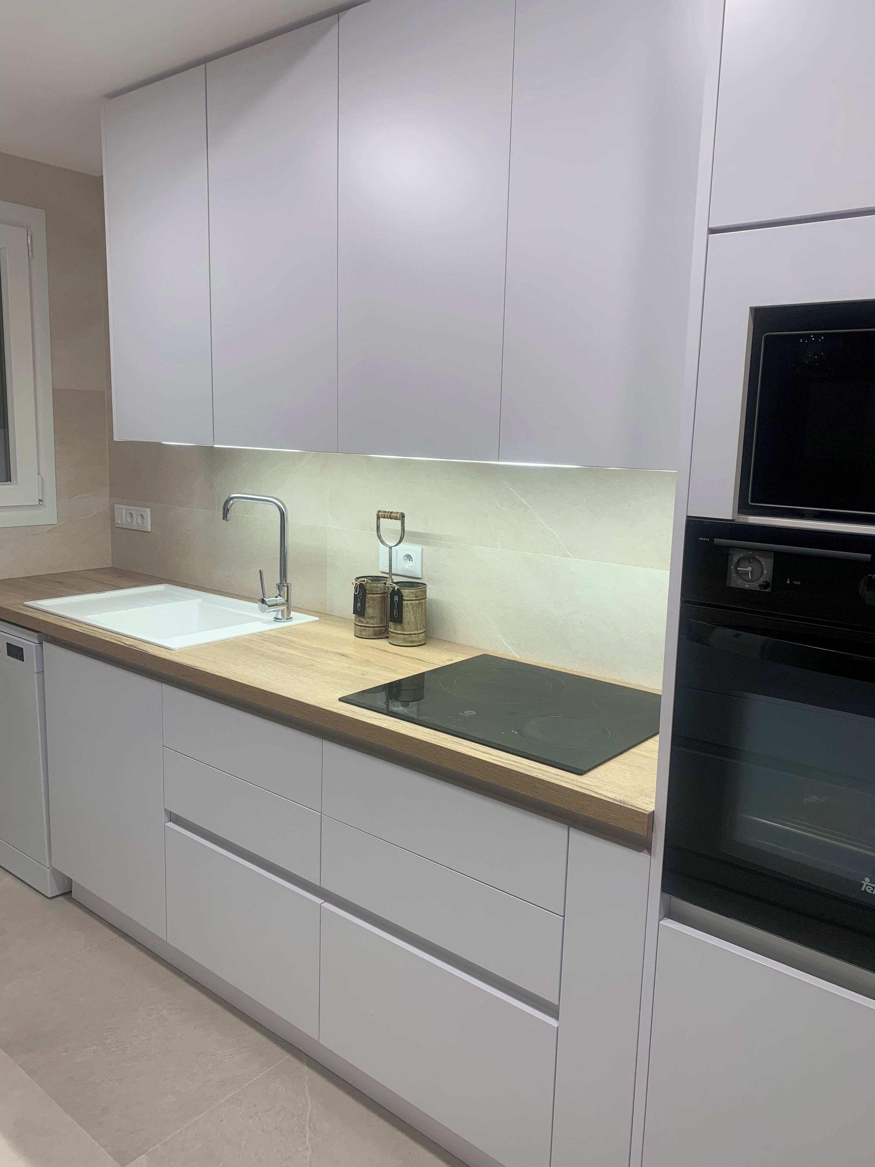 A modern kitchen with white cabinets, a double sink, a built-in oven, and a stainless steel range hood.