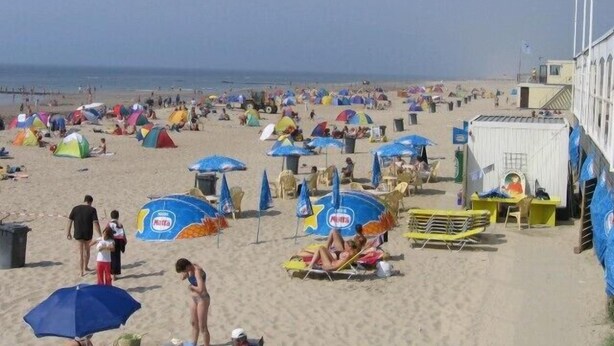 A beach with numerous colorful umbrellas and tents, a sandy shore, and a few people.