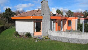 A modern house with a stone chimney, orange accents, and satellite dishes.