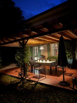 An outdoor dining area with a table and chairs, surrounded by greenery and a covered patio.