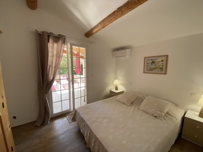 Ein Schlafzimmer mit einem Bett, einem Nachttisch, einer Klimaanlage, einem Fenster mit Vorhängen und einem Bild an der Wand.