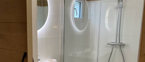 Een moderne badkamer met een douchecabine van glas, een houten wastafelmeubel en een spiegel met ronde verlichting.