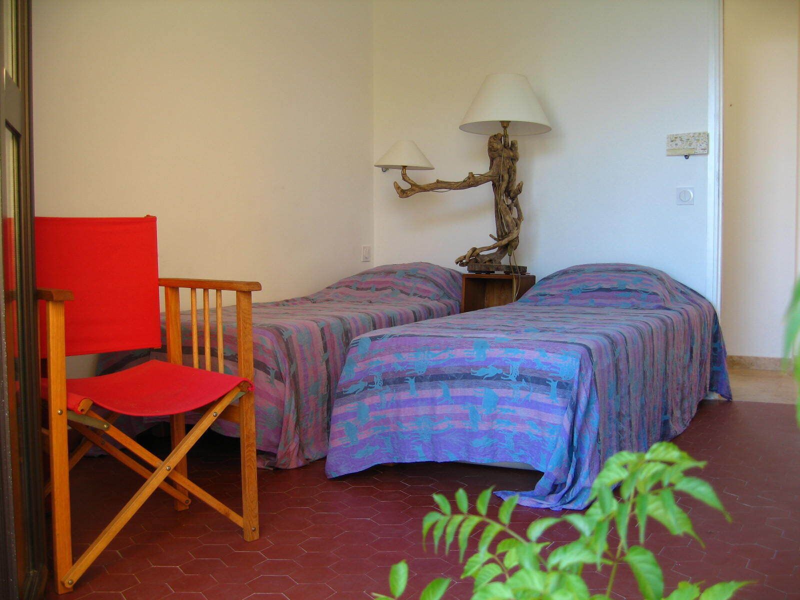 A room with two beds, a red chair, a lamp, and a plant.