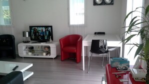 A modern living room with a flat-screen TV, a red chair, a white dining table, and a potted plant. - fully equipped apartment on the first floor (capbreton)