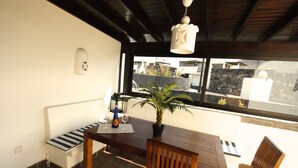 A dining area with a wooden table, two chairs, a bench, a potted plant, and a hanging light fixture.