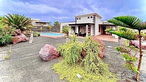 A modern house with a pool, surrounded by tropical plants and rocks.