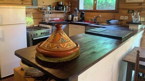 Cozinha com paredes de madeira, fogão, pia e janela com vegetação lá fora.