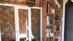 Quarto com piso de madeira, um banco com toalhas, estante de livros e porta com vidro trabalhado.