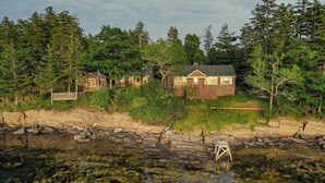 A cabin with a deck overlooking a rocky shoreline and dense forest. - Howard Family Cottage with Casco Bay Sunset Views! (Harpswell)