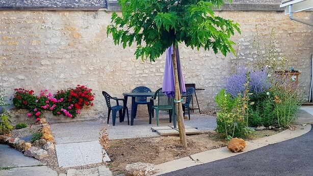 Une terrasse avec une table et des chaises, un petit arbre et diverses plantes.