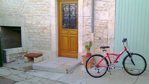 Un bâtiment en pierre avec une porte en bois, un vélo rouge et une plante en pot.