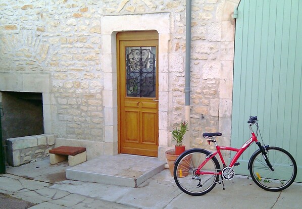 Un edificio de piedra con puerta de madera, una bicicleta roja y una planta en maceta.