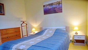 Une chambre à coucher comprenant un lit, deux tables de chevet avec des lampes, une commode en bois et un tableau accroché au mur.