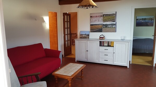Una sala de estar con un sofá rojo, una mesa de centro de madera, un armario blanco con libros y un cuadro colgado en la pared.