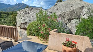 Um terraço com mesa e cadeiras de vidro, um vaso de plantas e vista para as montanhas.