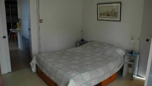 Ein Schlafzimmer mit einem Bett, einem Nachttisch, einer Wandlampe und einer Tür zu einem anderen Raum.