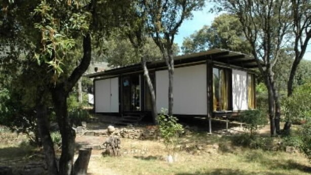 Eine kleine, eingeschossige Holzhütte im schlichten, rustikalen Stil, umgeben von Bäumen und einer natürlichen Landschaft.