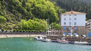 Una marina amb diverses embarcacions amarrades, un edifici blanc amb teulada vermella i una paret de pedra amb vegetació a l'esquena.