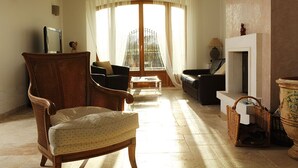 A living room with a large window, a fireplace, and a wicker chair. - Pretty farmhouse tastefully renovated, air-conditioned, in the vineyards, with jacuzzi pool (Ramatuelle)