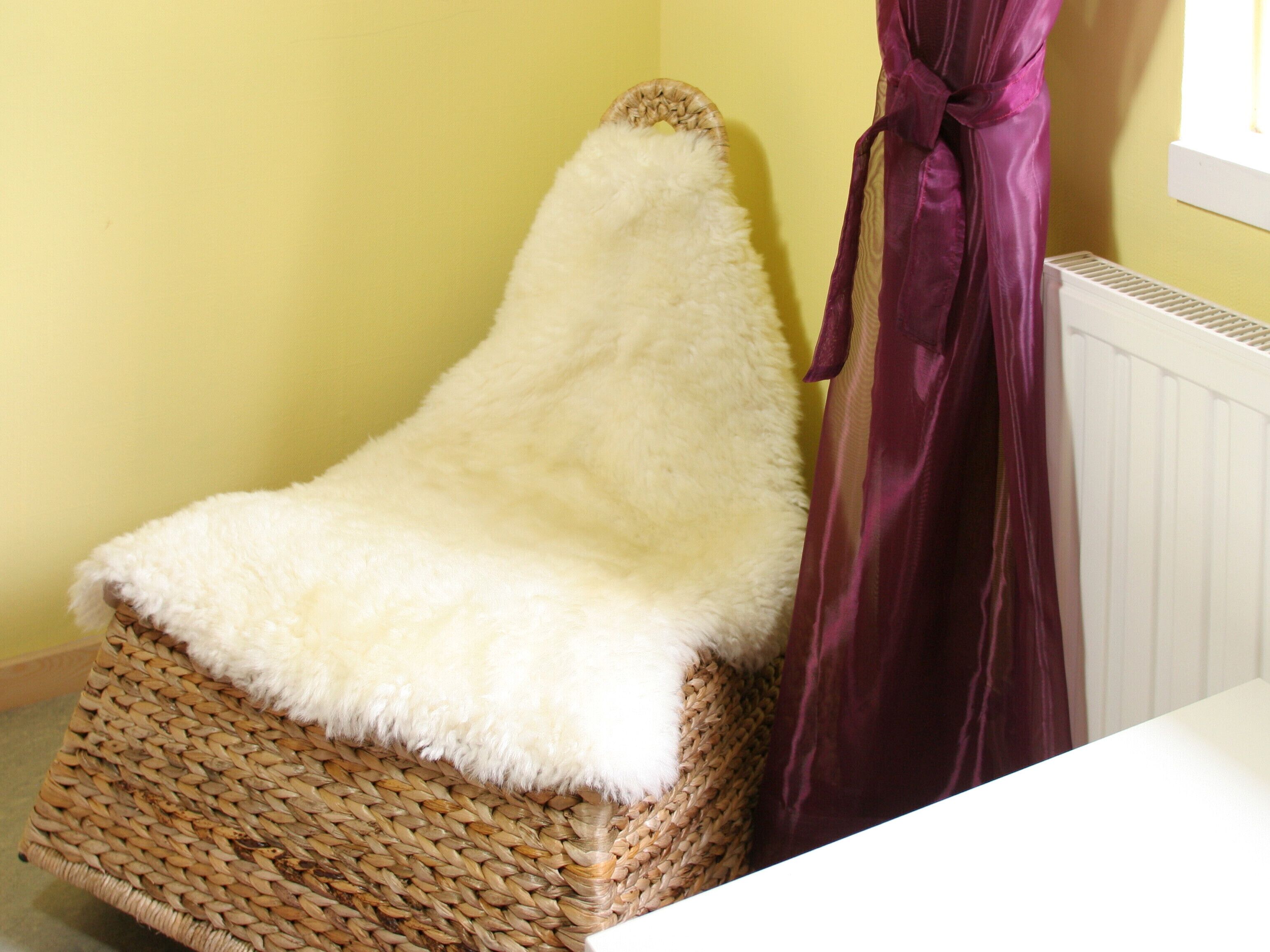 Una silla de mimbre con un edredón blanco y mullido, una cortina morada y un radiador blanco.