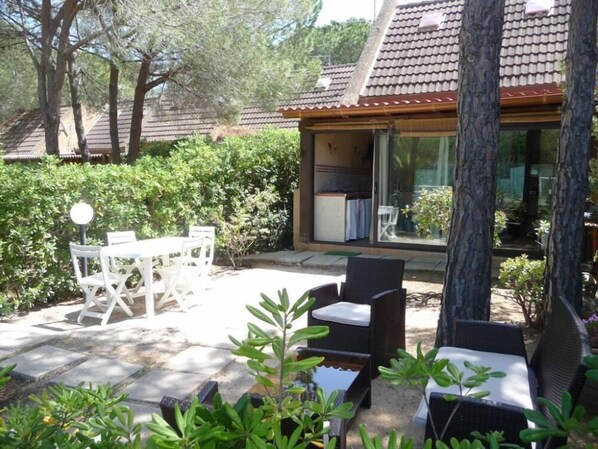 An outdoor patio area with a table and chairs, surrounded by greenery and trees.