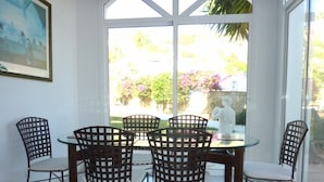 A dining area with a glass table and chairs, a white statue, and a view of a garden through large windows. - Spacious Villa With Sea And Mountain Views Very Close To The Communal Pool (Nerja)