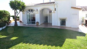 A modern house with a large glass door, a patio, and a well-maintained lawn. - Spacious Villa With Sea And Mountain Views Very Close To The Communal Pool (Nerja)