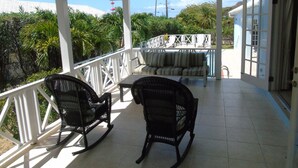 A covered outdoor area with two rocking chairs, a sofa, and a pool in the background. - Featured in Times Travel 50 Best Caribbean Villas Nov '14 (Hamilton Estate)