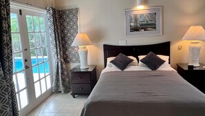 A bedroom with a bed, two bedside tables with lamps, a framed picture on the wall, and a view of a swimming pool through a glass door. - Featured in Times Travel 50 Best Caribbean Villas Nov '14 (Hamilton Estate)