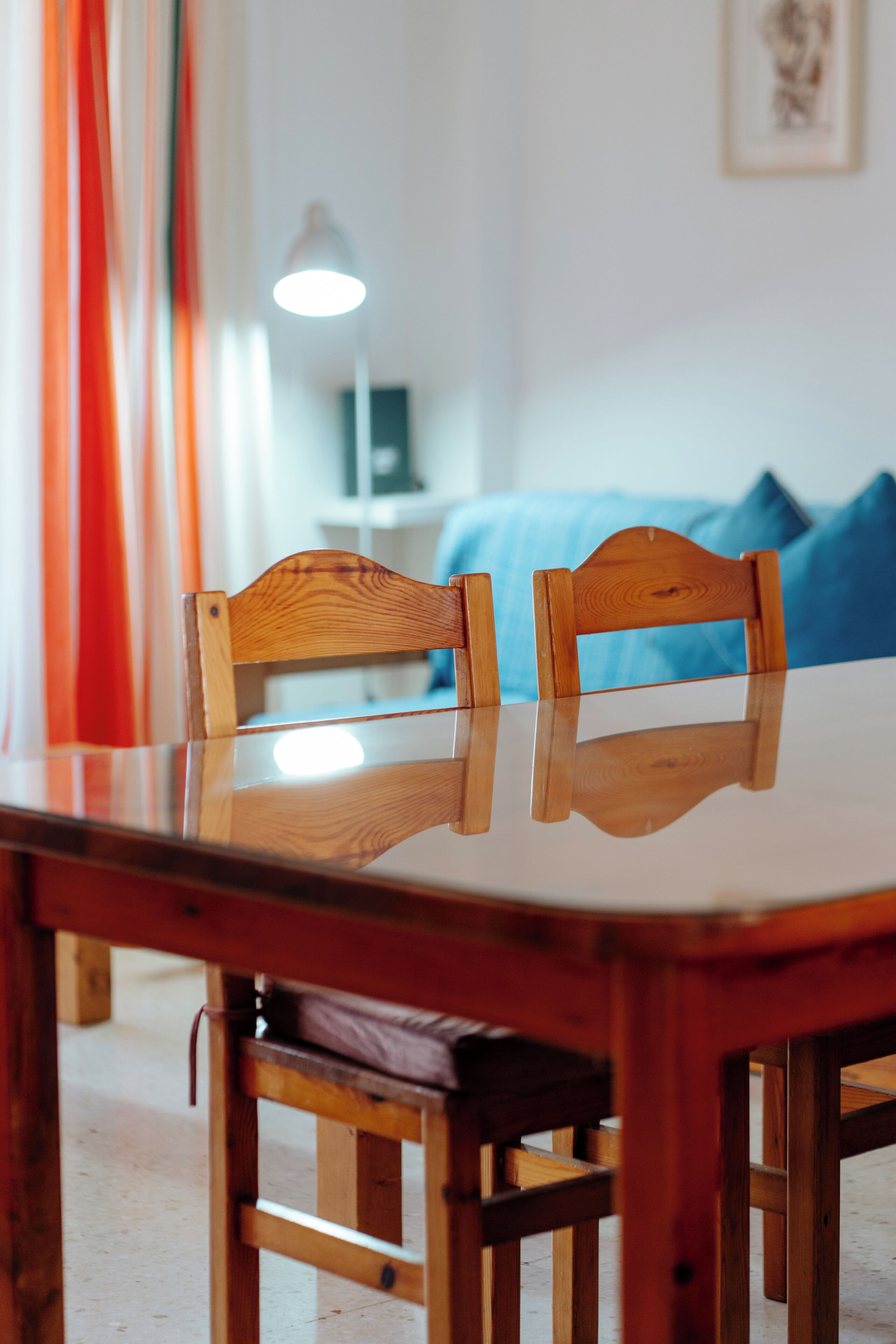 Une table à manger en bois avec deux chaises, une lampe en arrière-plan et un lit avec une literie bleue.
