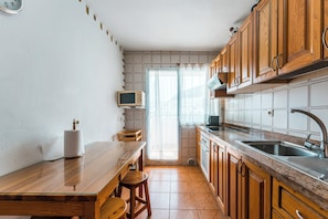 Eine Küche mit Holzausstattung, einer Edelstahl-Spüle, einer Mikrowelle und einem Fenster mit Vorhängen.