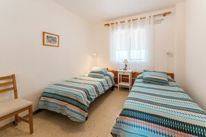 A room with two single beds, a desk, a chair, and a window with curtains.