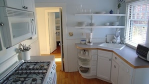 A kitchen with white cabinets, a stove, a coffee maker, and a window with blinds.