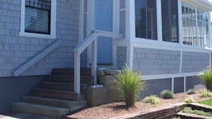 A house with a covered porch, a set of stairs leading to the entrance, and a small garden area with shrubs.