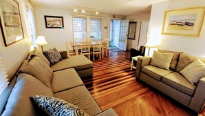 A living room with a sectional sofa, a smaller sofa, a dining table with chairs, and a wooden herringbone floor.