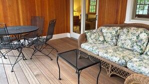 Un patio cubierto con una mesa redonda de metal y sillas, un sofá de mimbre y un ventanal corredero que da a un espacio interior.
