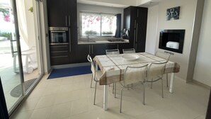 A modern kitchen with dark cabinets, a built-in oven, and a dining area with a table and chairs. - Sea Front Villa with Private Pool - Free WiFi (Santa Maria di Leuca)
