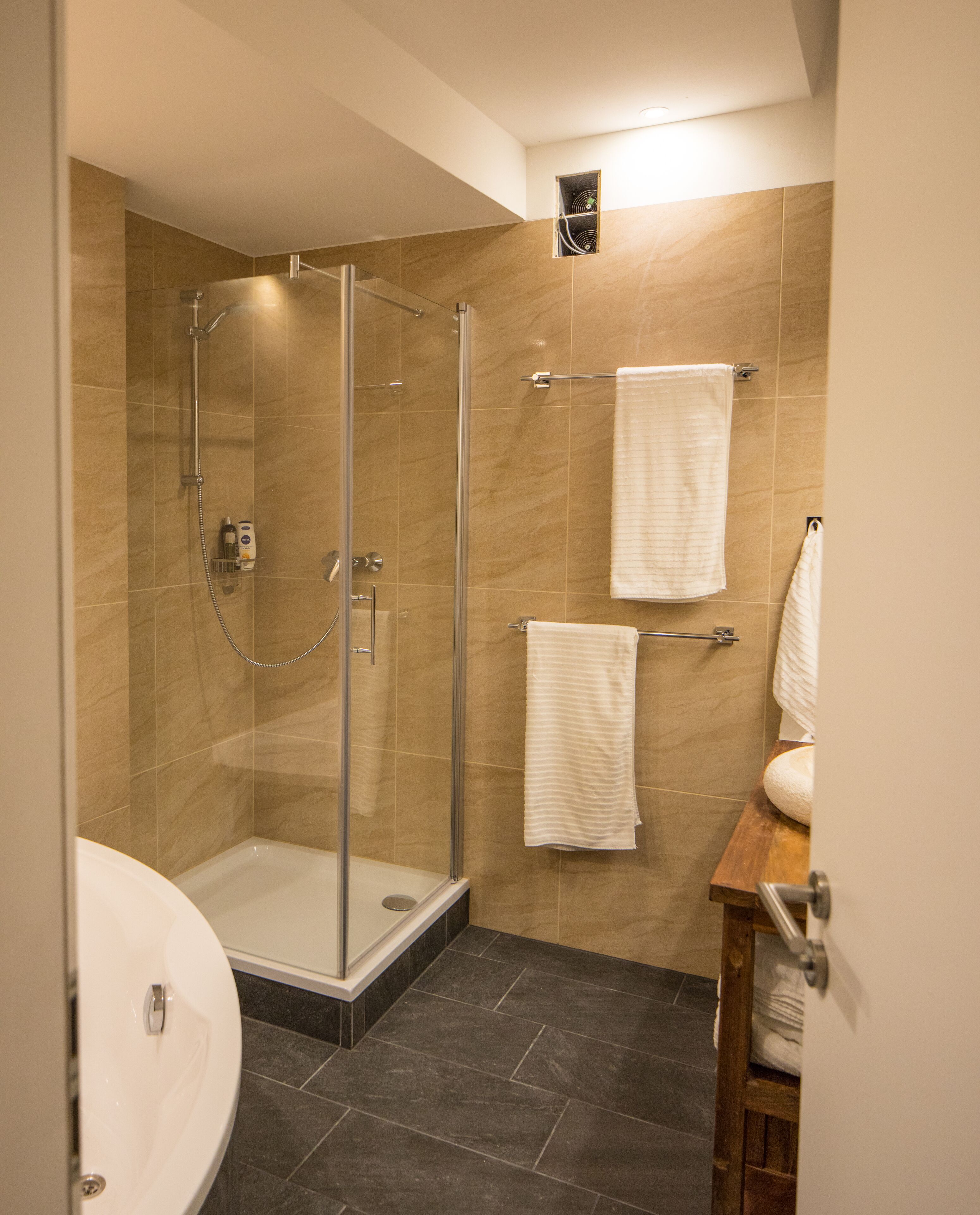 Ein modernes Badezimmer mit einer gläsernen Duschkabine, einer Holzbk und zwei weißen Handtüchern an Handtuchhaltern.
